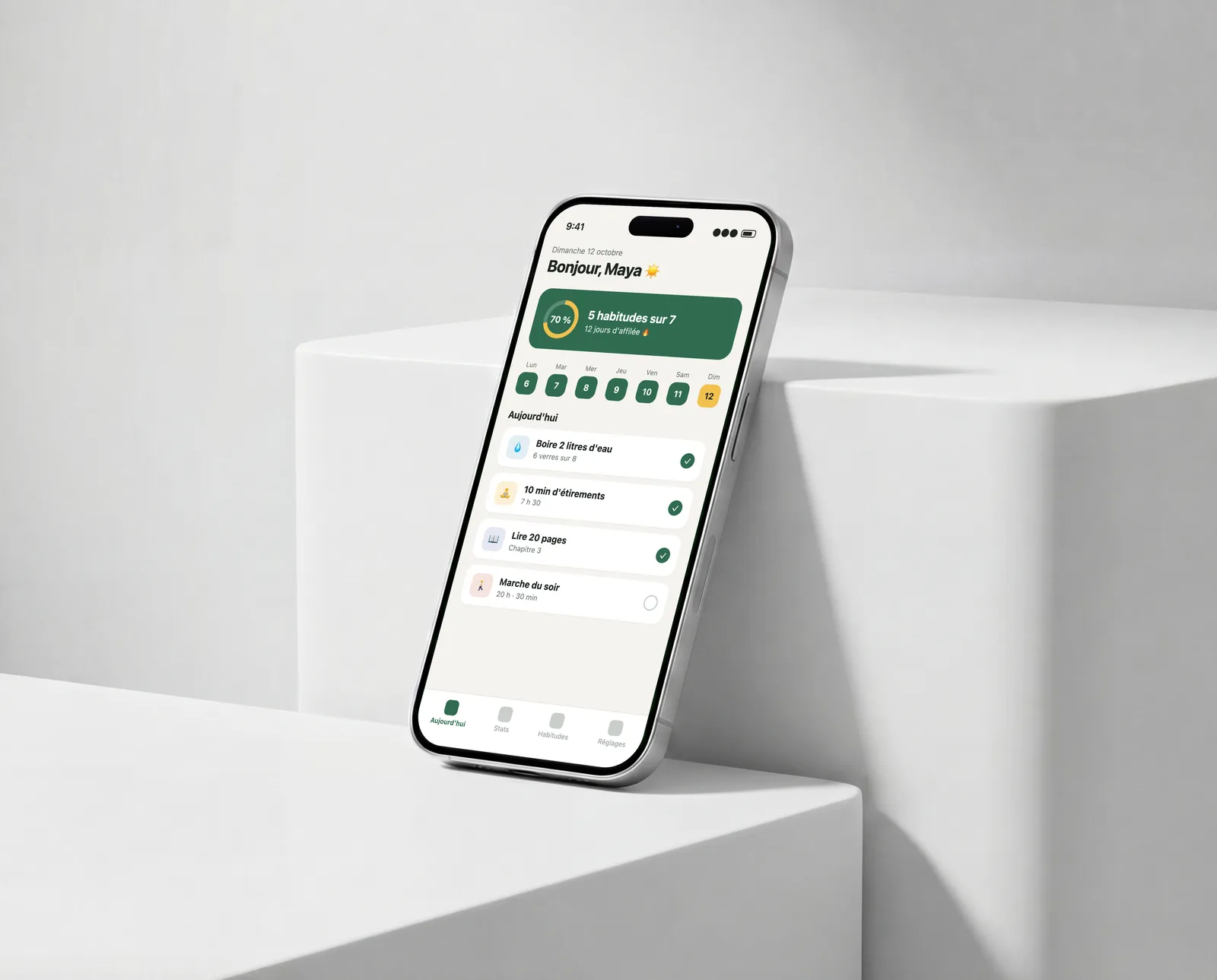 iPhone posé contre un socle blanc dans un studio lumineux, affichant une appli de suivi d'habitudes