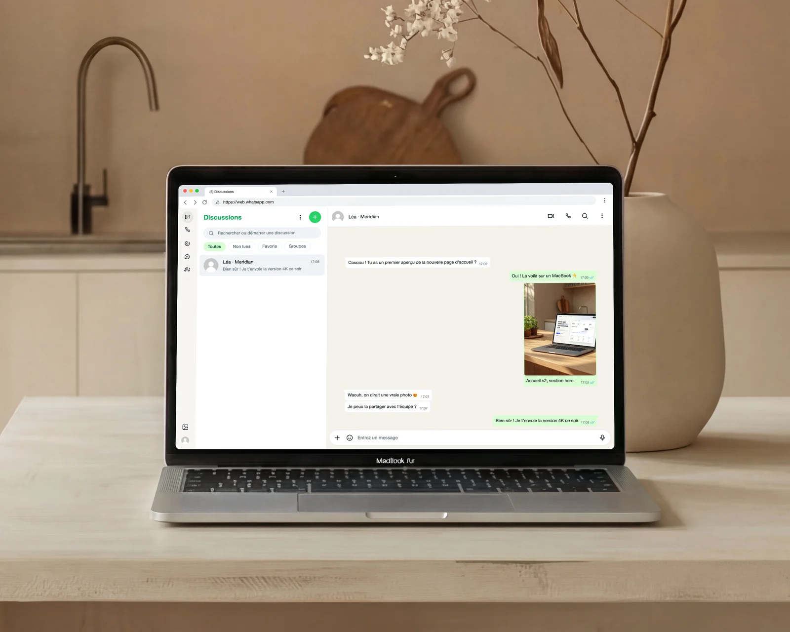 MacBook sur un plan de travail en bois clair dans une cuisine minimaliste affichant la même conversation dans WhatsApp Web