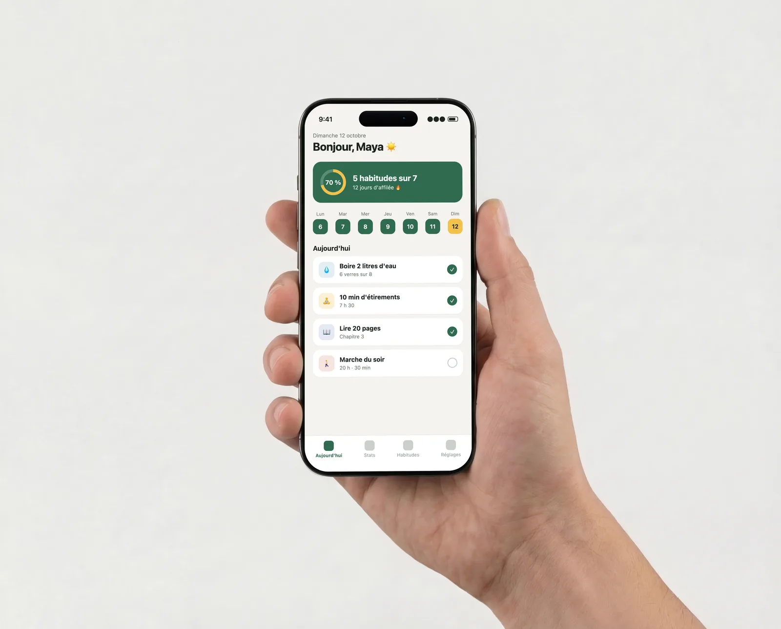 iPhone tenu d'une main devant un mur clair, affichant une appli de suivi d'habitudes à 70 % de la journée