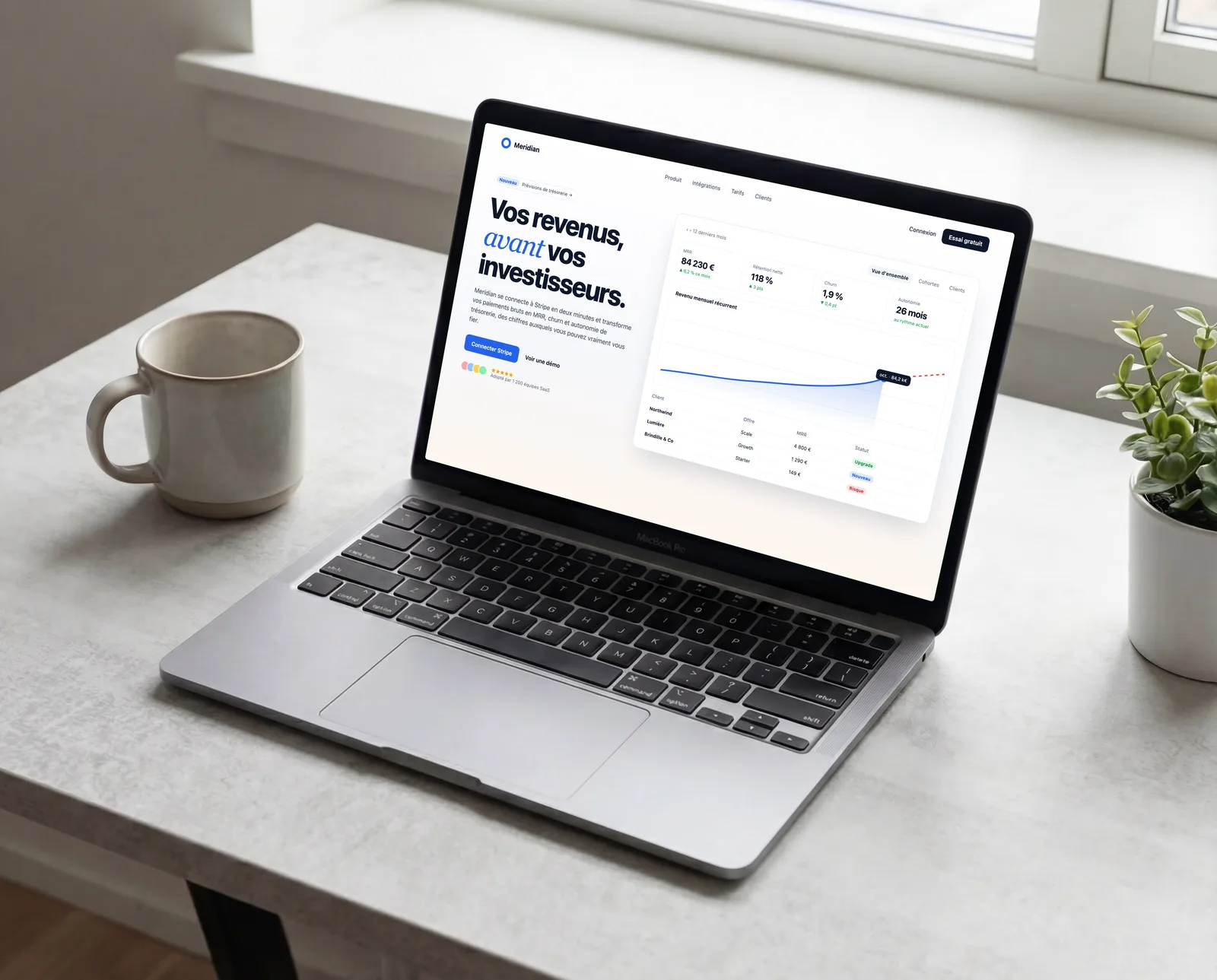 MacBook Pro de trois quarts sur un bureau en béton près d'une fenêtre, affichant la landing page d'un SaaS avec une courbe de revenus