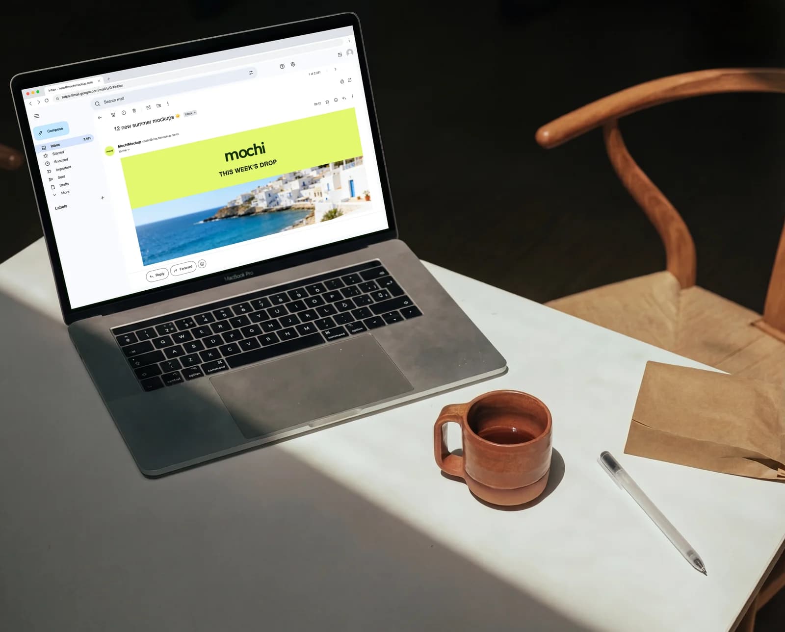 MacBook on a white café table showing the same newsletter opened in Gmail on the web, folders on the left